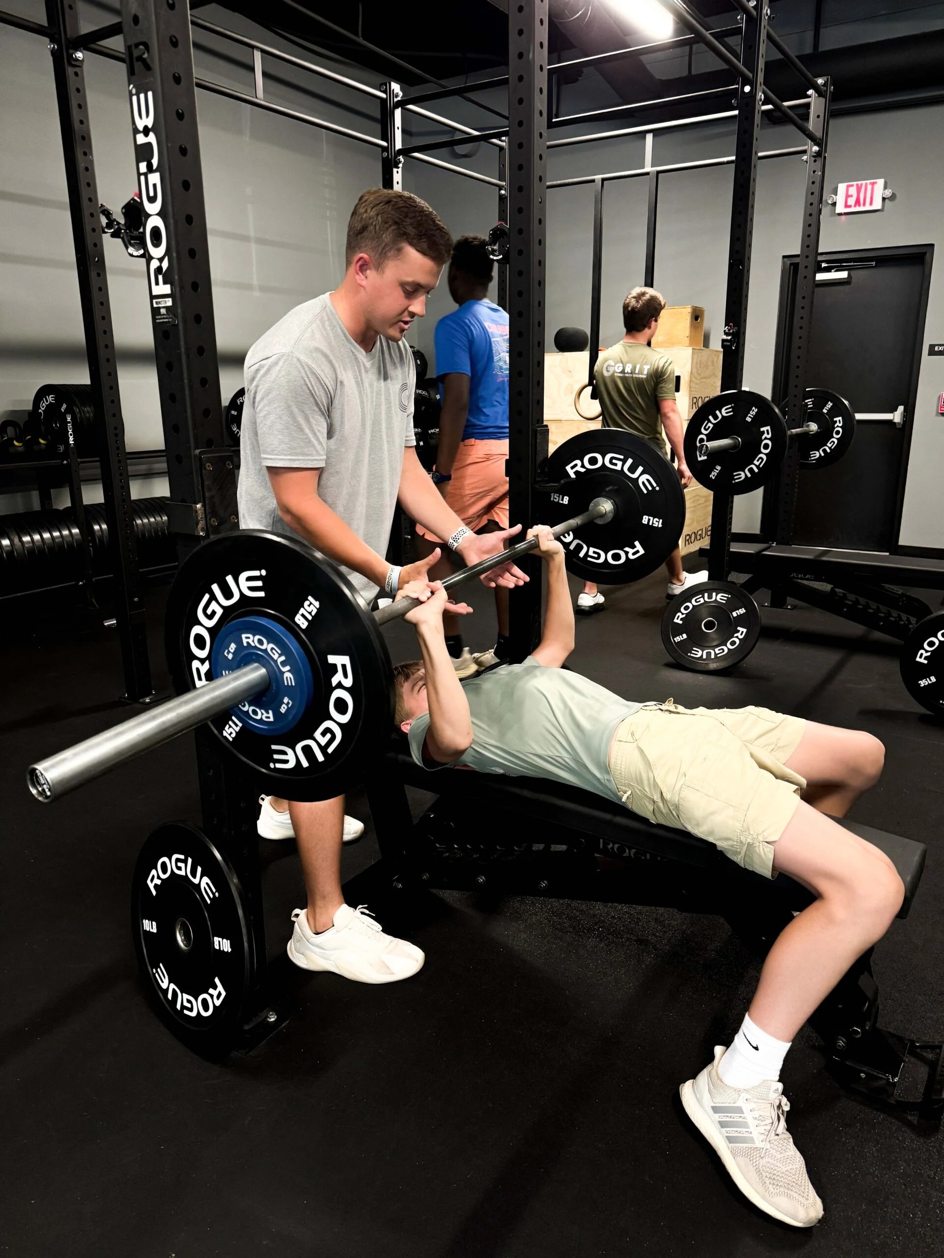 A GRIT coach spotting a young athlete during a bench press inside the Auburn training facility